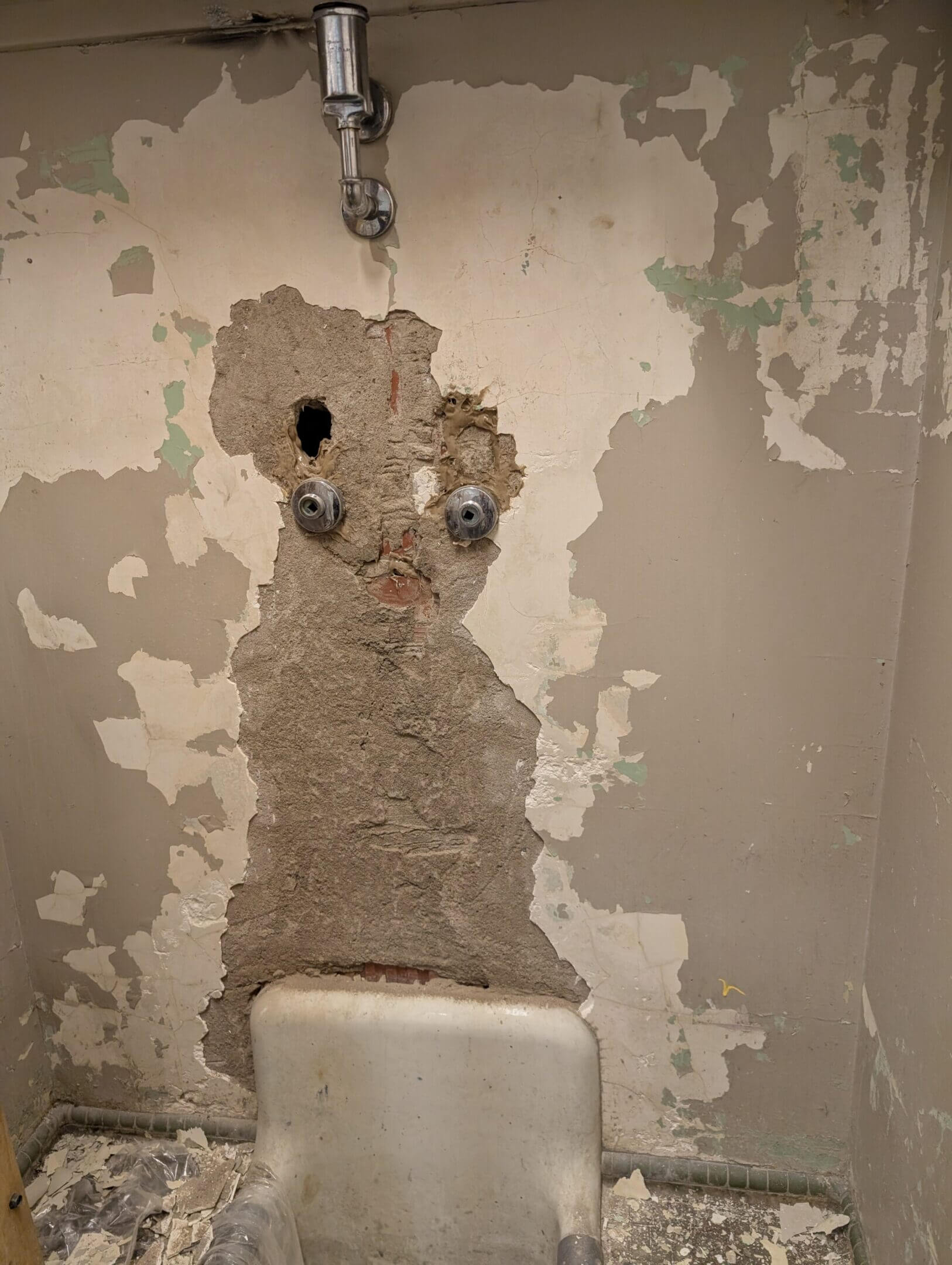Wall paint peeling to reveal an eye-like pattern above a toilet.