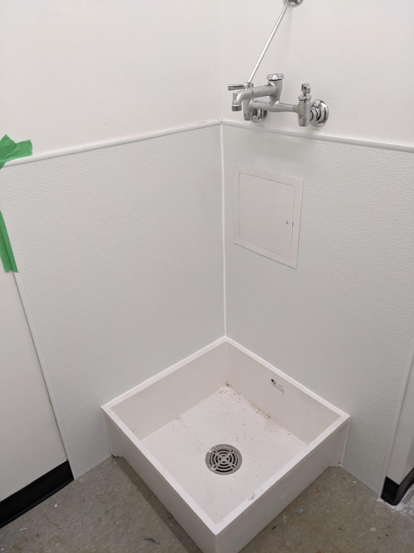 A clean white utility sink with a mop nearby and wall faucets above.