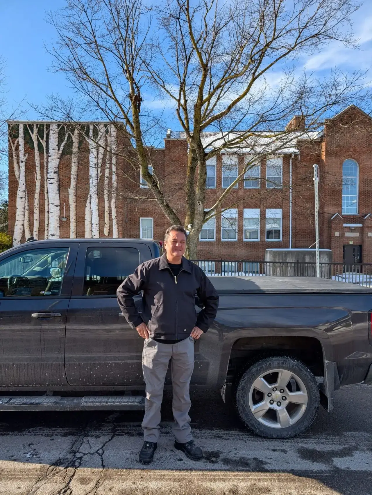 Person standing confidently by a black pickup truck in front of a brick building.